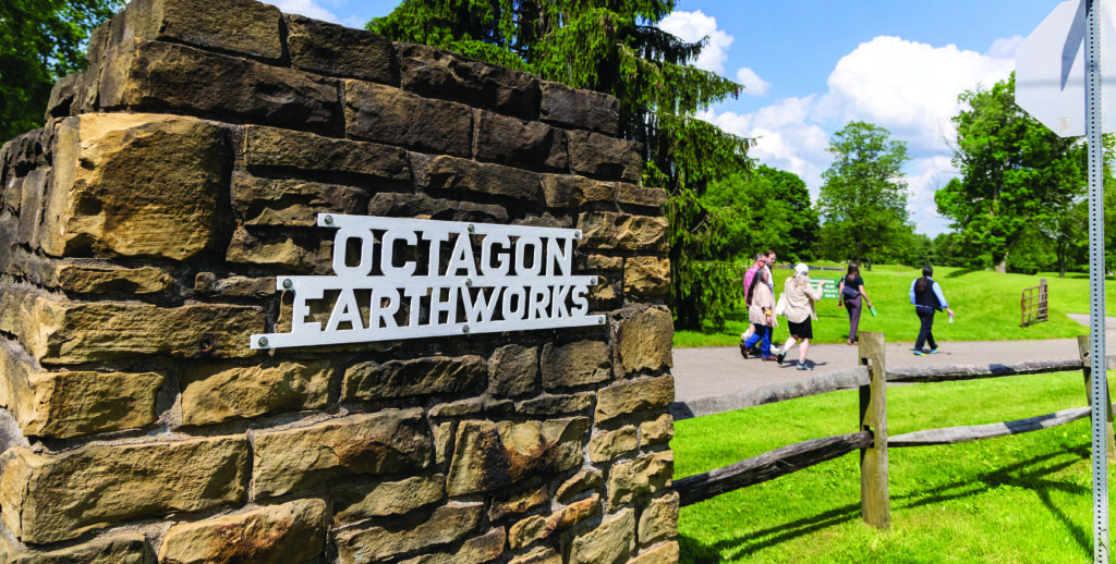 People walk past a sign for the Octagon Earthworks in Newark, Ohio. Photo by Christopher Dawson.