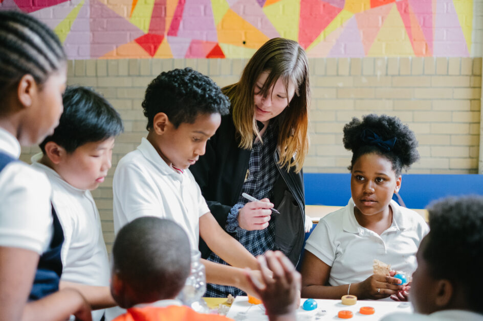 A group of children and a teacher gathered around a table making art.